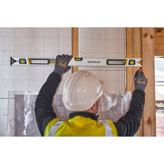 STANLEY FMHT43674-1 spirit level in use on wall by worker with gloves and hard hat, construction site setting.
