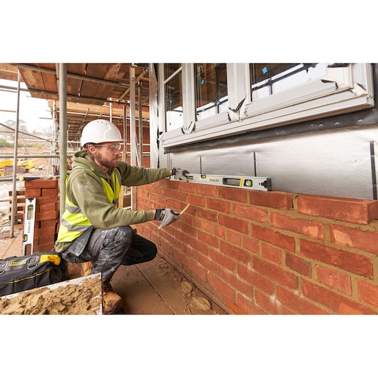 STANLEY FMHT43675-1 spirit level used by a worker to check brick wall alignment at a construction site.