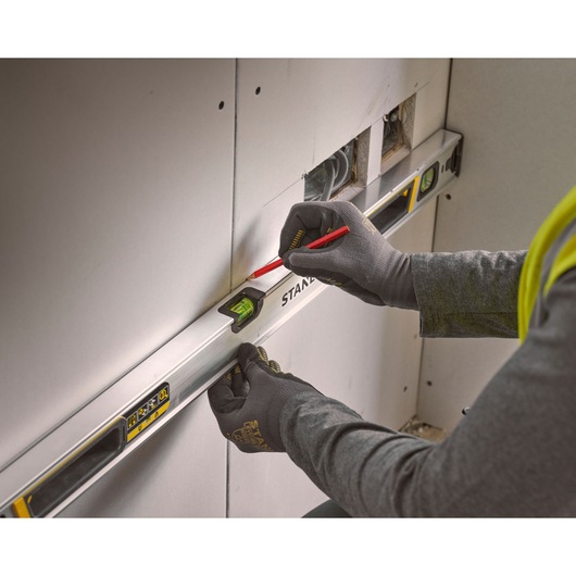 Photo of STANLEY FMHT43675-1 spirit level in use against drywall, worker marking line with pencil.