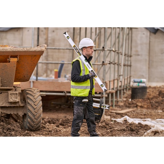 Photo of STANLEY FMHT43675-1 spirit level held by worker at construction site, yellow and black accents visible.