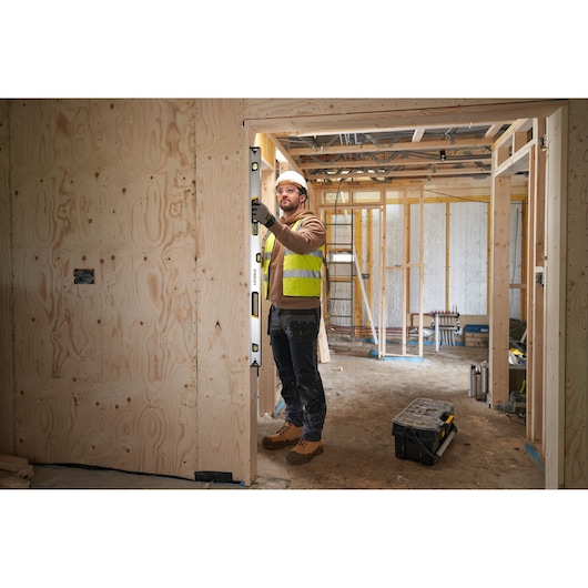 Photo of worker using STANLEY FMHT43676-1 spirit level on wooden door frame at building site, toolbox on floor.