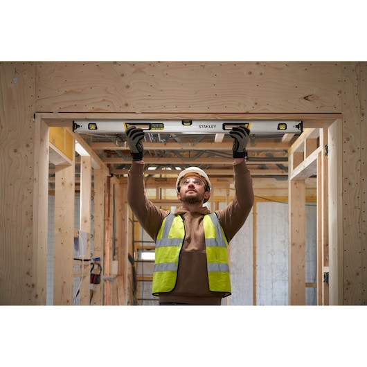 Photo of worker using STANLEY FMHT43676-1 spirit level on door frame in wooden construction site.
