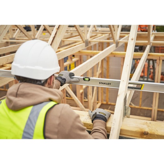 STANLEY FMHT43679-1 spirit level used by worker with gloves and hard hat on wooden roof construction site.