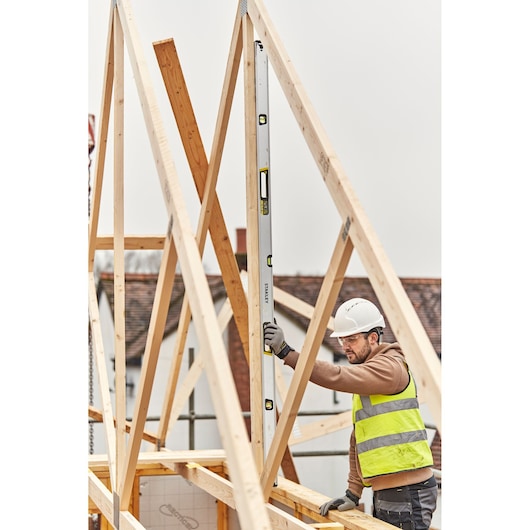 STANLEY FMHT43680-1 spirit level held vertically by worker at construction site with timber framing.