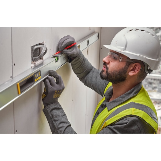 STANLEY FMHT43680-1 spirit level used by worker marking wall, construction context, side angle.