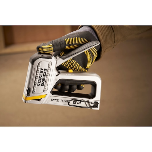 Photo of STANLEY FMHT70250-0 multi-tacker staple gun held in a gloved hand, close-up side view.