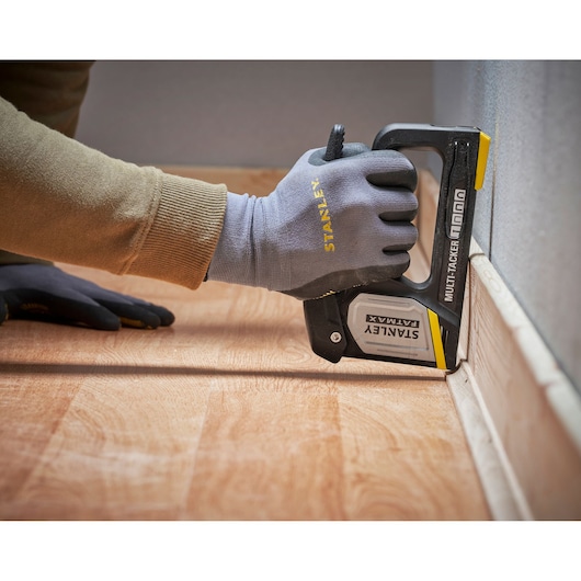 STANLEY FMHT70401-0 multi-tacker stapler in use securing flooring near wall, shown in close-up.