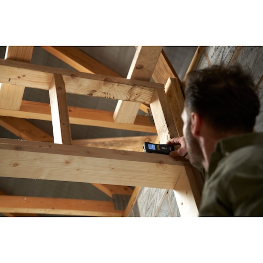 STANLEY FMHT77165-0 laser distance measurer used by person to measure wooden beam in construction setting.