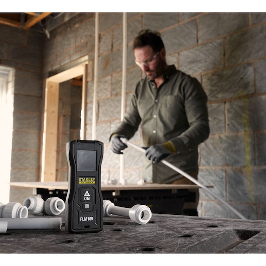 Photo of STANLEY FMHT77165-0 laser measure on a workbench at a construction site with pipes and fittings.