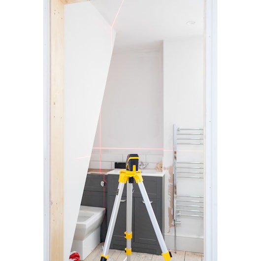 STANLEY FMHT77585-1 laser level on tripod in bathroom, projecting red horizontal and vertical lines.