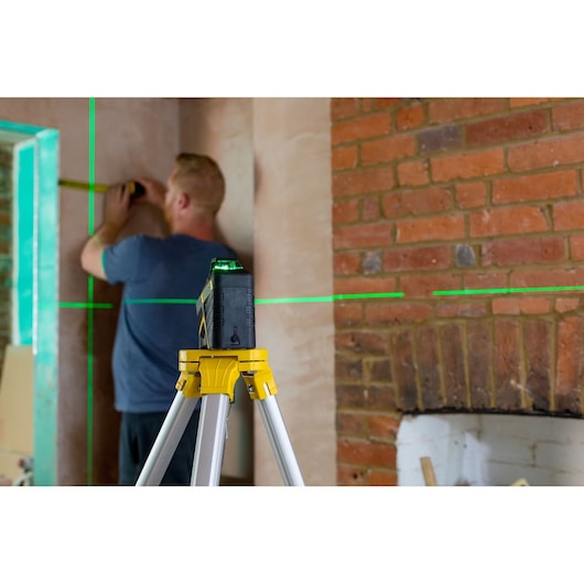 STANLEY FMHT77617-1 laser level on tripod projecting green lines, used for interior wall measurement.