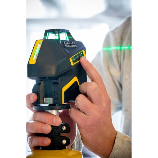 Photo of STANLEY FMHT77617-1 laser level being operated by a hand, showing illuminated control panel and green laser line.
