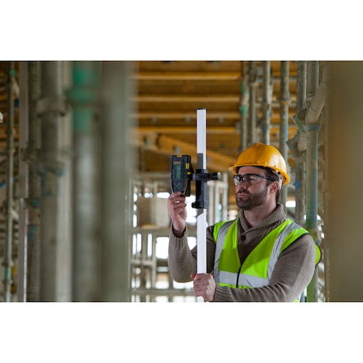 STANLEY FMHT77653-0 laser detector on staff held by worker in safety vest and helmet at construction site