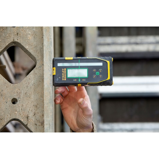 STANLEY FMHT77653-0 laser detector held against concrete by hand, construction site background.