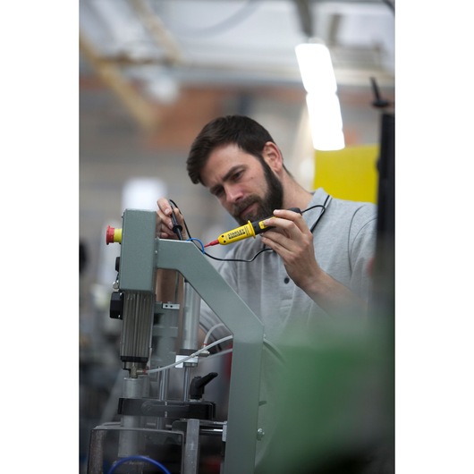 Photo of STANLEY FMHT82566-0 voltage tester in use, worker checking machine wiring in industrial setting.