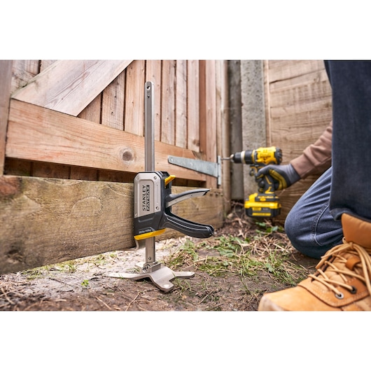 Photo of STANLEY FMHT83550-1 door installation clamp used to hold a wooden gate, shown outdoors during assembly.