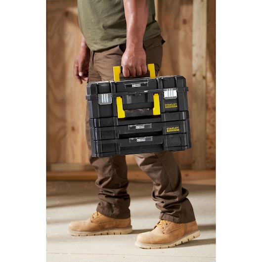 STANLEY FMST1-71981 black stackable tool box with yellow handle, carried by worker, product in use.