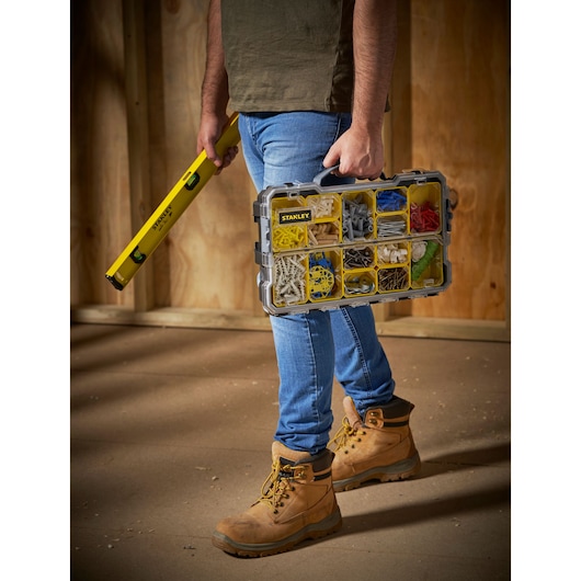 STANLEY FMST1-75779 organiser box with compartments, held by person, side angle, construction site.