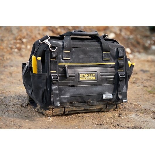 STANLEY FMST17627-1 tool bag with yellow trim and pockets, photographed outdoors on dirt.