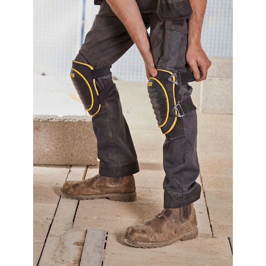 Photo of STANLEY FMST82961-1 knee pads worn over work pants, black with yellow trim, on construction site.