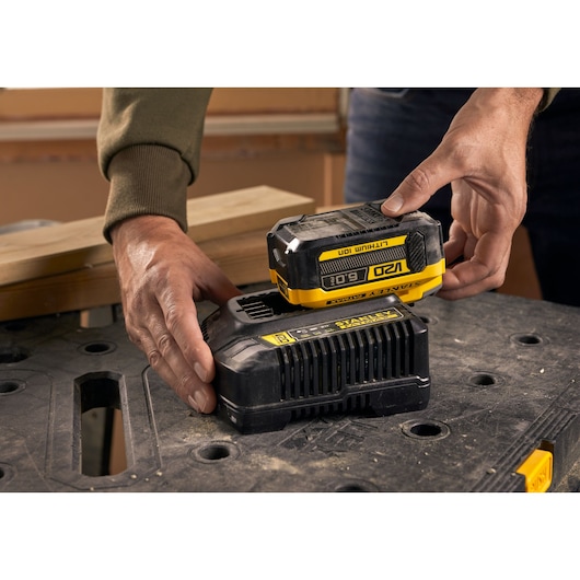 STANLEY SFMCB206 battery being placed on charger, close-up on black work surface.