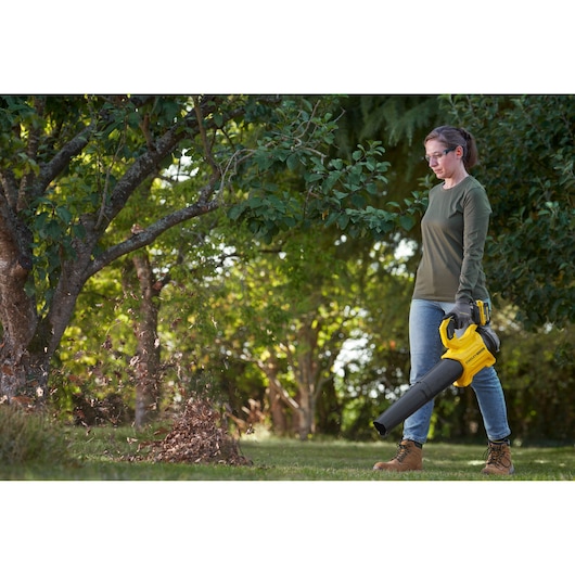 STANLEY SFMCBL730M1 leaf blower in use outdoors, yellow and black handheld cordless tool blowing leaves.