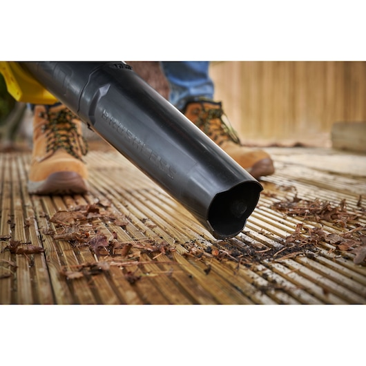 STANLEY SFMCBL730M1 leaf blower nozzle in use on wooden decking, blowing dry leaves and debris.