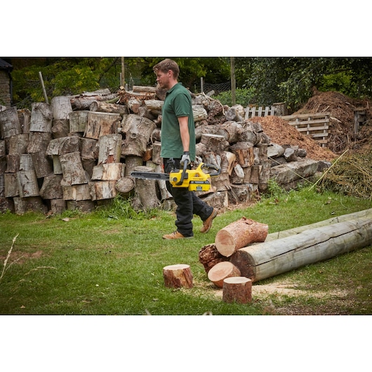 STANLEY SFMCCSB664B chainsaw held by person outdoors near cut logs and stacked firewood.