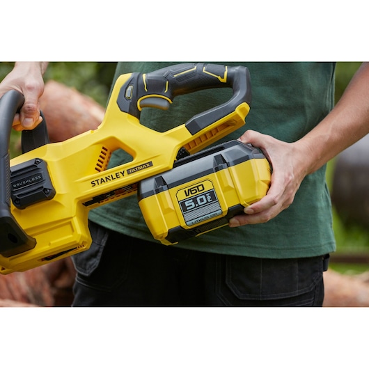 Photo of STANLEY SFMCCSB664B V60 5.0Ah cordless chainsaw held by person outdoors.