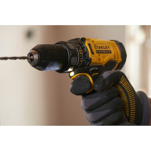 STANLEY SFMCD700C2K cordless drill held by gloved hand, yellow and black body, side angle.