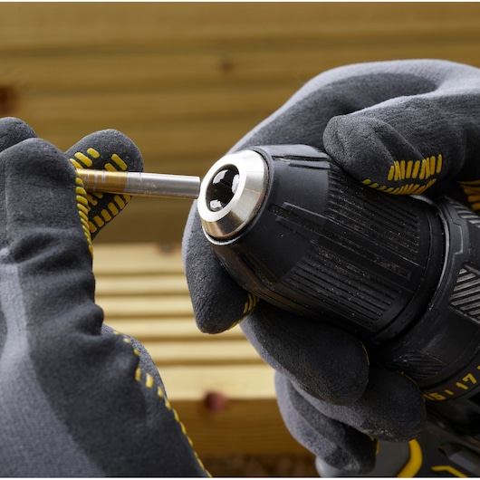 STANLEY SFMCD700C2K drill close-up with gloved hands inserting a metal bit, outdoor setting.