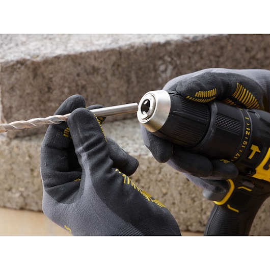 STANLEY SFMCD711D22 drill held with gloves, close-up of inserting drill bit outdoors.
