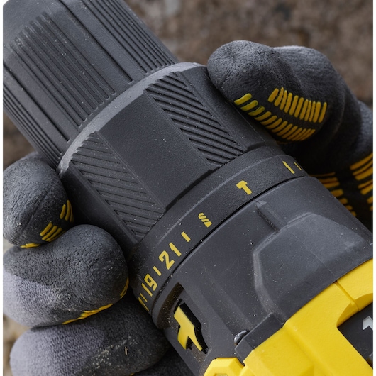 Close-up of STANLEY SFMCD711D22 drill settings dial held by gloved hands, showing numbers and symbols.