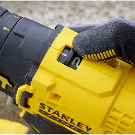 Photo of STANLEY SFMCD711D22 drill mode switch being adjusted by gloved hand, yellow and black color, closeup.