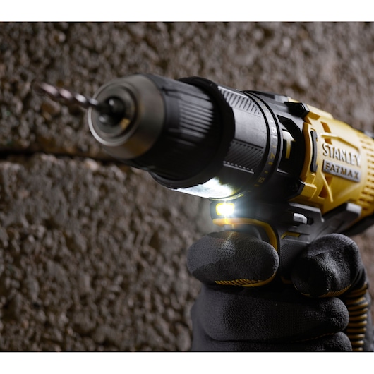 STANLEY SFMCD711D22 cordless drill in use, close-up side angle, yellow and black body, LED light on.