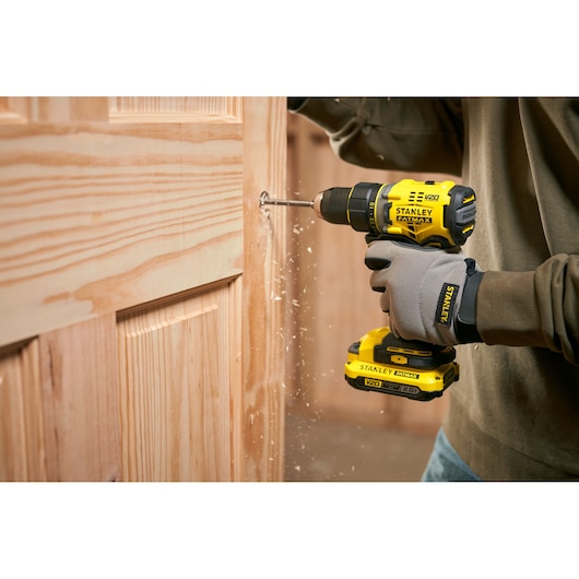 Photo of STANLEY SFMCD720D2K cordless drill in use, drilling into a wooden door, close-up angle.