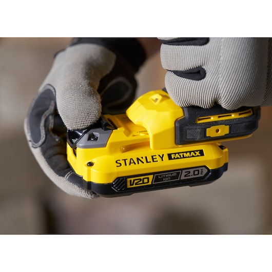 Close-up photo of STANLEY SFMCD721B power tool with yellow FATMAX V20 2.0Ah lithium-ion battery being held by gloved hands.