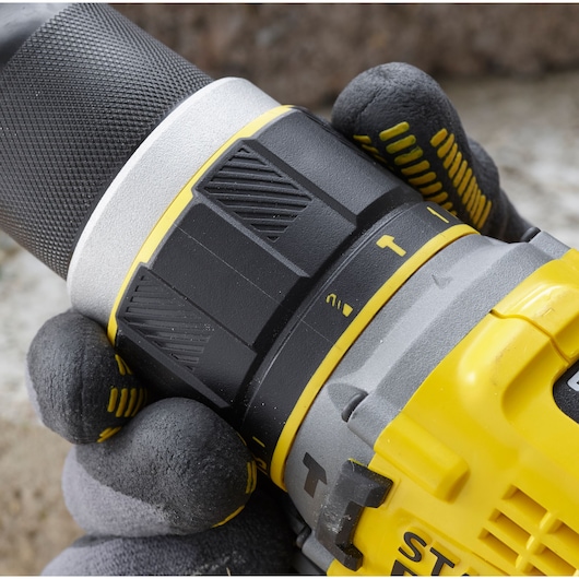 Photo of STANLEY SFMCD721M2K drill close-up, yellow and black body, textured grip, glove hand.