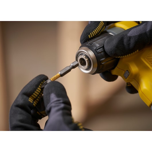 STANLEY SFMCD750B drill photography, close-up of gloved hands inserting bit into yellow drill chuck.
