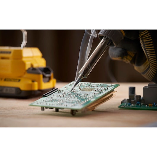 STANLEY SFMCE040B soldering tool in use on electronic circuit board, close-up photo with visible smoke.