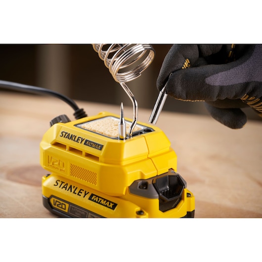 Photo of STANLEY SFMCE040B soldering station with yellow V20 battery, metal holder, and tools on a workbench.