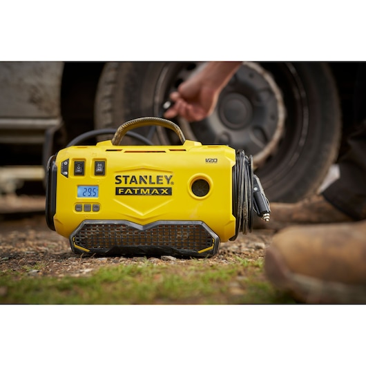 STANLEY SFMCE520B portable yellow tire inflator with digital display, shown outdoors near a car wheel.