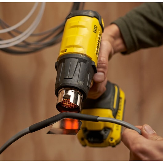 Photo of STANLEY SFMCE530B cordless heat gun in use heating a cable.