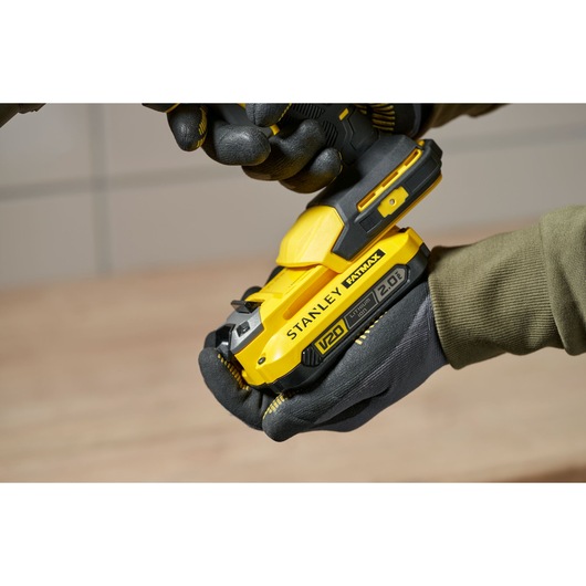Photo of STANLEY SFMCE600B yellow cordless tool in gloved hands, close-up side view.