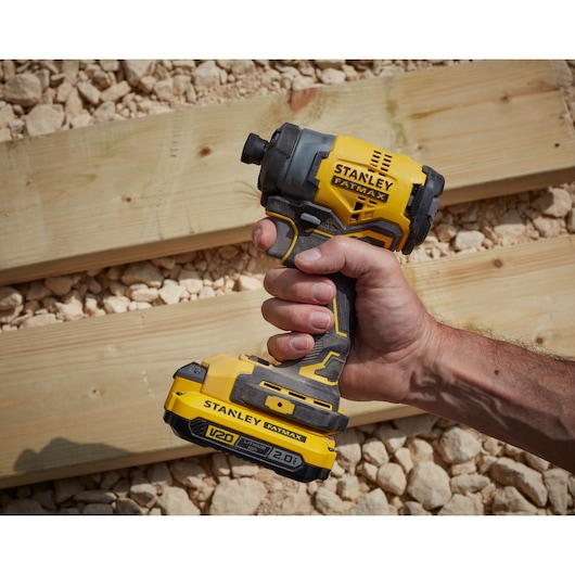 STANLEY SFMCF810B cordless impact driver held in hand, yellow black, used near wooden planks outdoors.