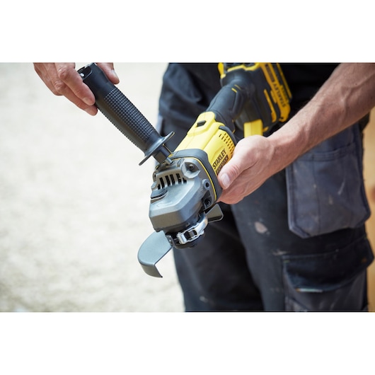 STANLEY SFMCG400M2K angle grinder held in hands, yellow and black body, being assembled outdoors.