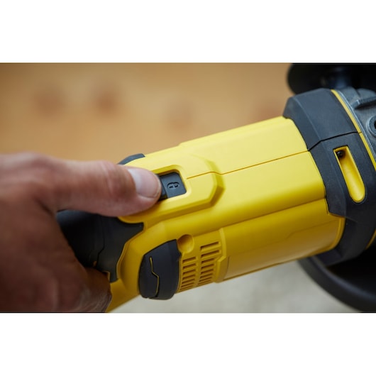 Photo of a hand operating the STANLEY SFMCG400M2K angle grinder power switch, showing yellow and black tool details.