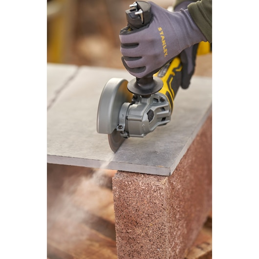 STANLEY SFMCG700B angle grinder cutting stone slab, close-up photo with safety glove.
