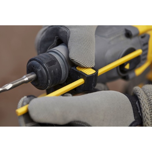 STANLEY SFMCH900B rotary hammer drill close-up, gloved hand adjusting yellow depth gauge, side angle.