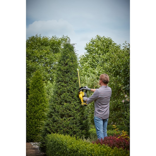 STANLEY SFMCHT855M1 hedge trimmer used outdoors by a person trimming a tall bush.